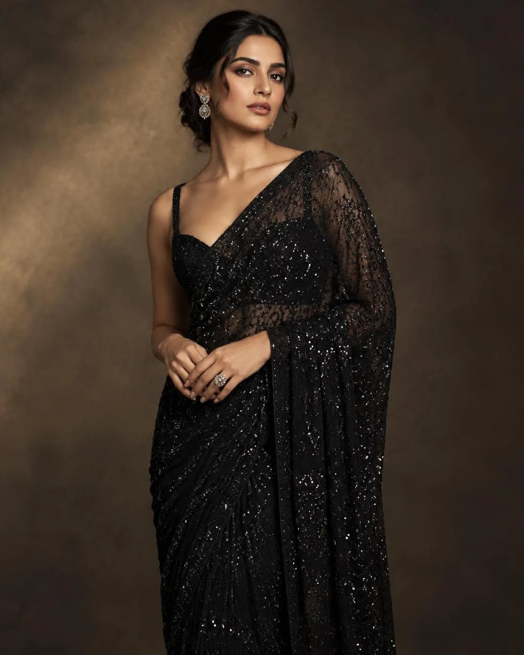 Model in a black sequin-embroidered georgette saree against a warm studio backdrop