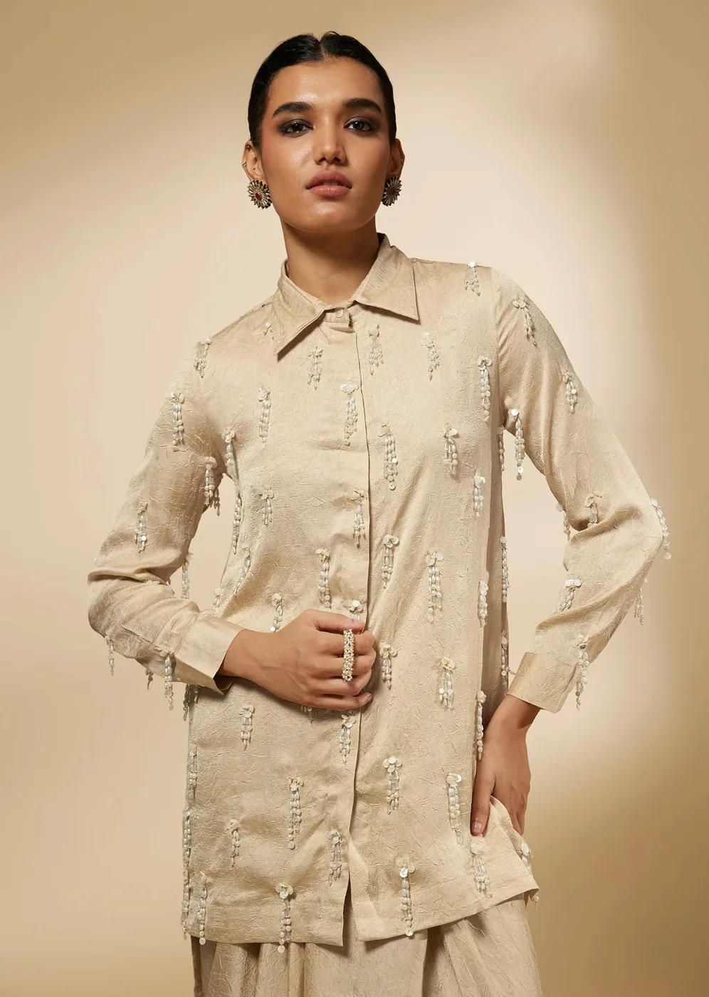 Model in a beige crepe shirt and skirt set with embellished tassels
