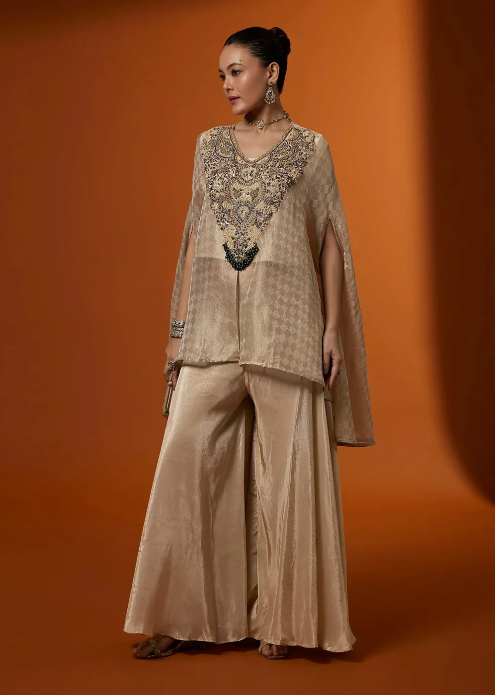 Model in a gold tissue kurta and palazzo set against a rust backdrop